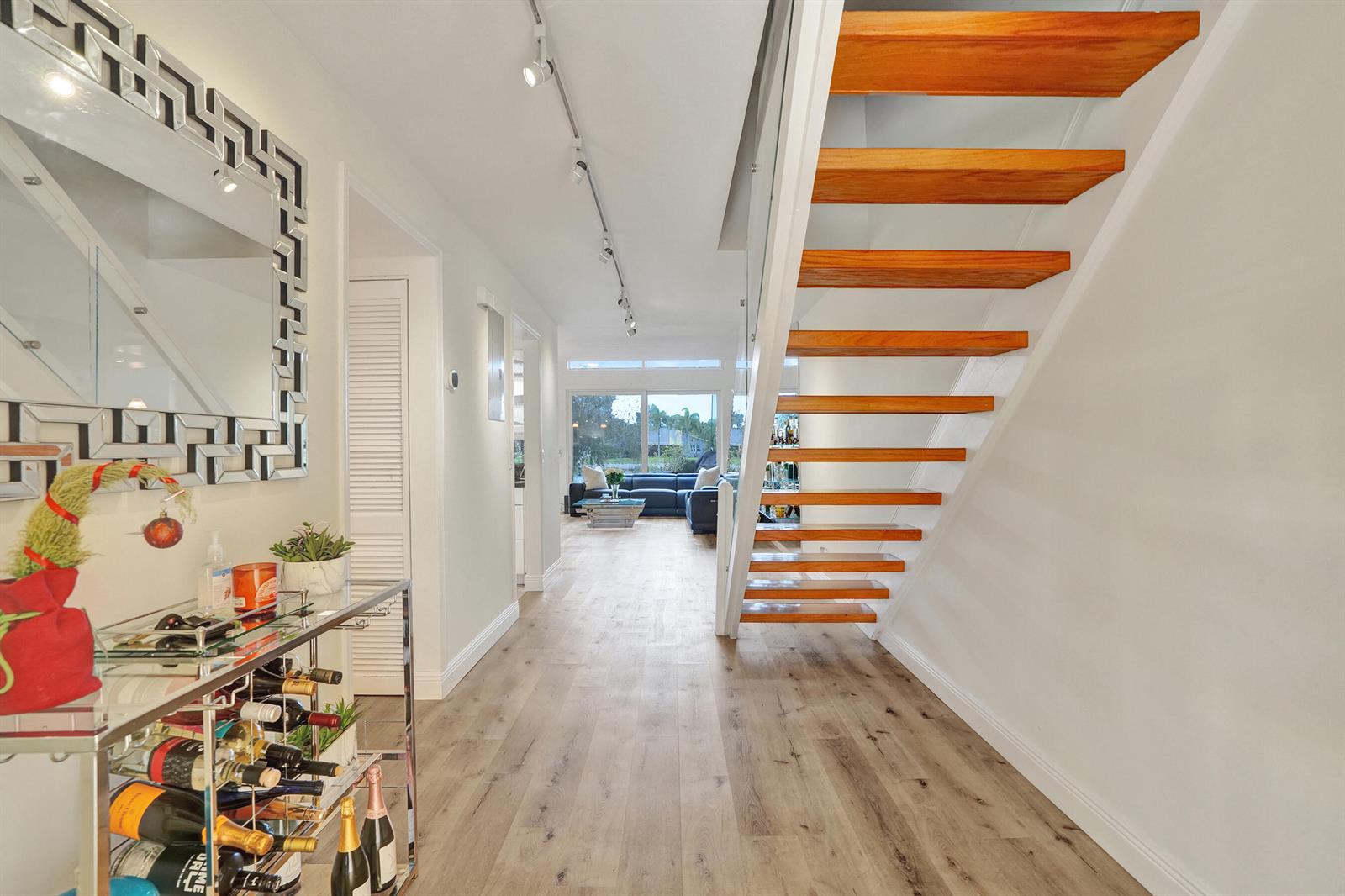 A hallway features light wood flooring, a floating staircase, and a bar cart — 1122 NW 79th Drive, Plantation FL 33322, PLANTATION, FL