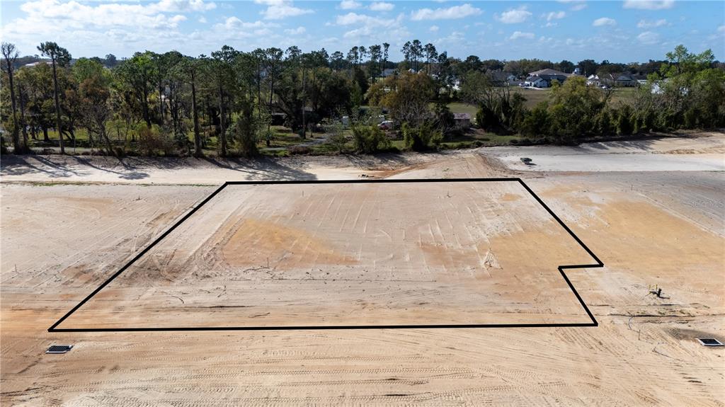 An aerial view shows a cleared, rectangular residential lot outlined in black on a sunny day — 32886 DUNNE ROAD, SAN ANTONIO, FL