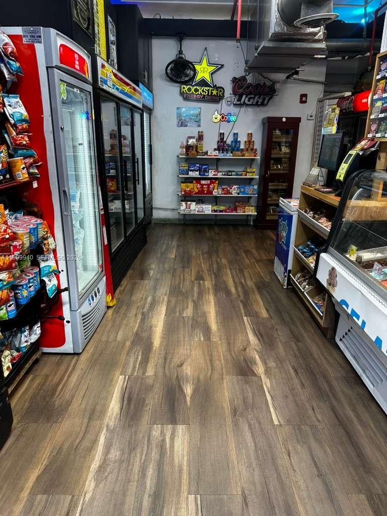A small convenience store interior features wood-look flooring, glass-front refrigerators, and various retail display shelves — Collins Ave, Miami Beach FL 33139, MIAMI BEACH, FL
