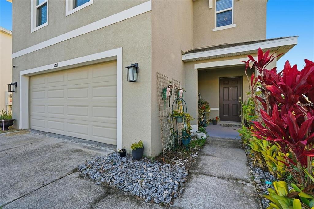 The exterior of a two-story house features a beige stucco facade, a garage, and landscaping — 7811 DAVIE RAY DRIVE, ZEPHYRHILLS, FL