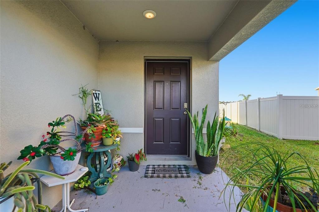 A covered front porch features a dark brown door, potted plants, and a welcome mat — 7811 DAVIE RAY DRIVE, ZEPHYRHILLS, FL