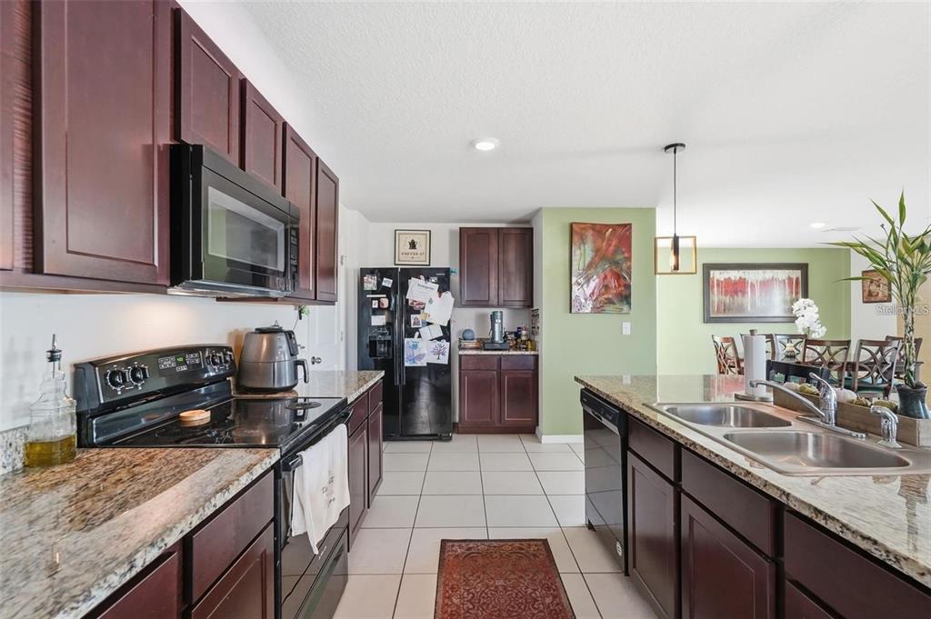 A kitchen with dark wood cabinets, granite countertops, stainless steel appliances, and tile flooring — 7811 DAVIE RAY DRIVE, ZEPHYRHILLS, FL