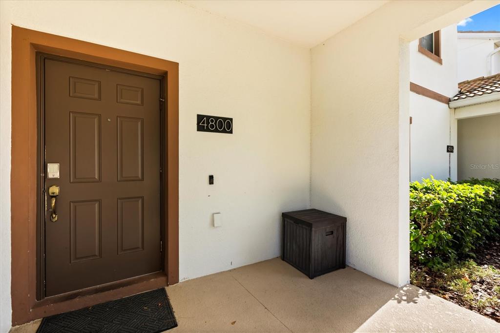 A brown front door with a house number sign sits on a covered concrete porch — 4800 CRUSOE STREET, KISSIMMEE, FL