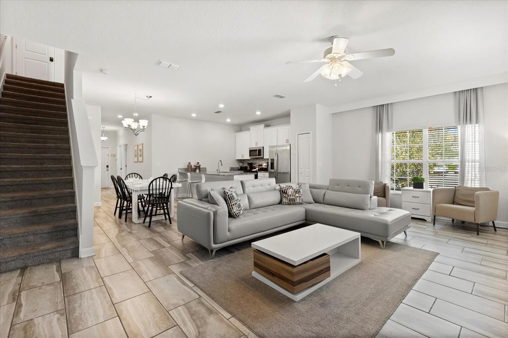 An open-concept living and dining area features tile floors, a gray sectional, and a staircase — 4800 CRUSOE STREET, KISSIMMEE, FL
