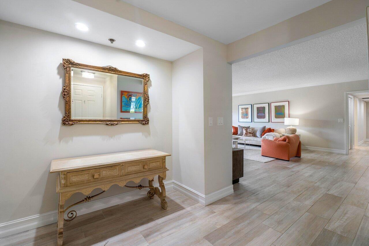 A foyer with a wooden console table and ornate mirror leads into a living room — 950 De Soto Road # 2b, Boca Raton FL 33432, BOCA RATON, FL