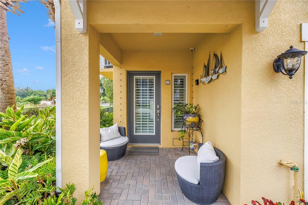 A covered entryway features a gray door, two wicker chairs, and a paved floor — 6149 ANCHORAGE WAY S, ST PETERSBURG, FL