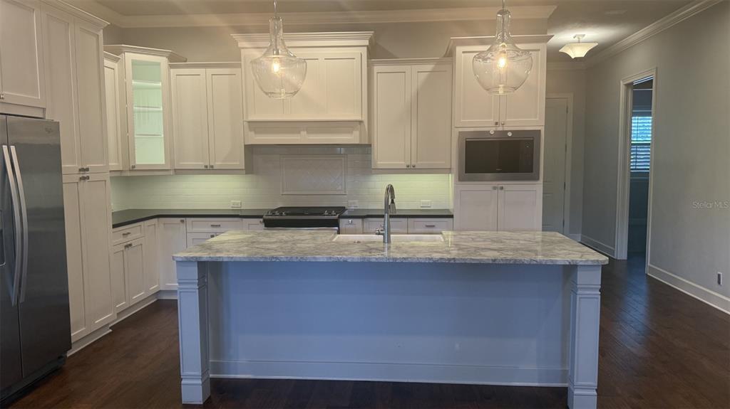 A kitchen features white cabinetry, a marble-topped island, stainless steel appliances, and dark wood flooring — 636 SW 128TH TERRACE, NEWBERRY, FL