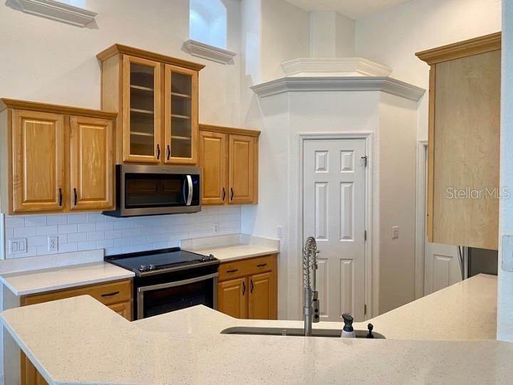 A kitchen features light wood cabinets, white countertops, a subway tile backsplash, and stainless appliances — 5224 HAMMOCK POINTE COURT, ST CLOUD, FL