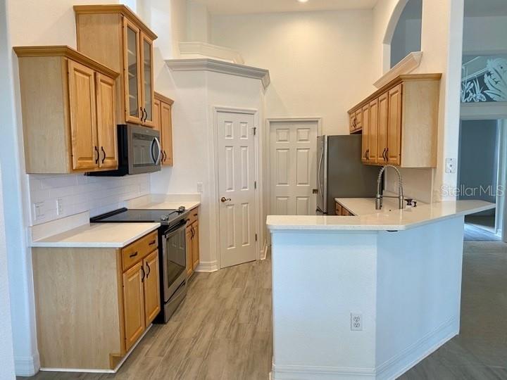 A kitchen features light wood cabinets, white countertops, stainless steel appliances, and wood-look flooring — 5224 HAMMOCK POINTE COURT, ST CLOUD, FL