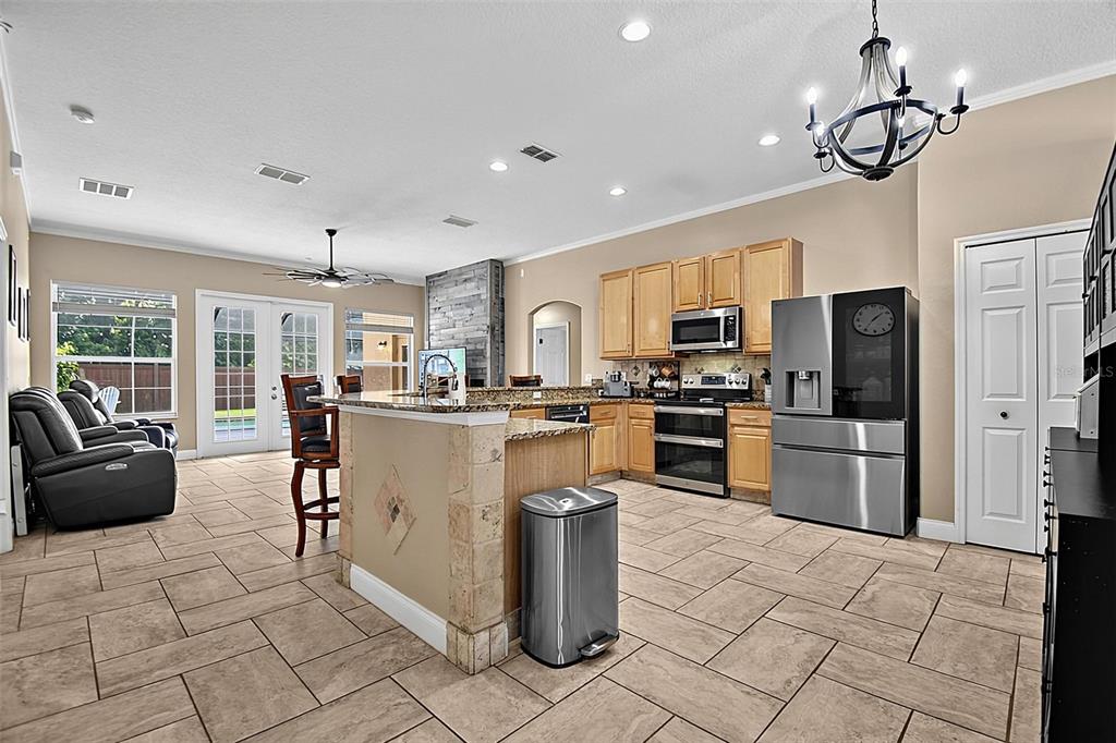 A kitchen with light wood cabinets, stainless steel appliances, and tile flooring opens to a living area — 61 FRANCIS LN, PALM COAST, FL