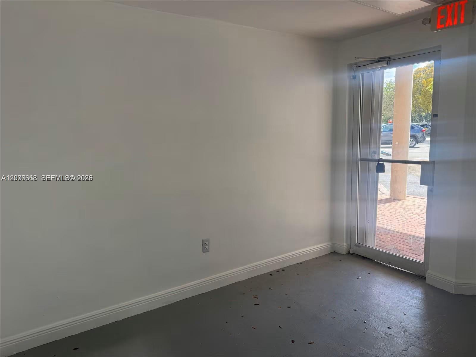 An empty room features white walls, a gray floor, and a glass door with an exit sign — 10171 NW 58th St # 11, Doral FL 33178, DORAL, FL