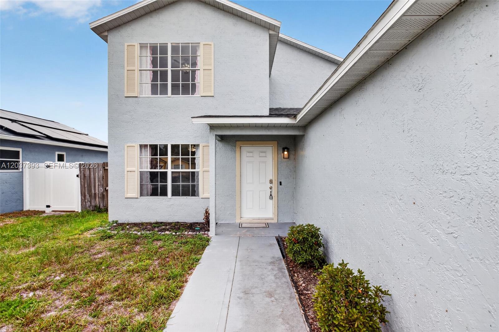 The exterior of a two-story house features light gray stucco walls and a white front door — 1951 TROPIC BAY CT, Orlando FL 32807, ORLANDO, FL