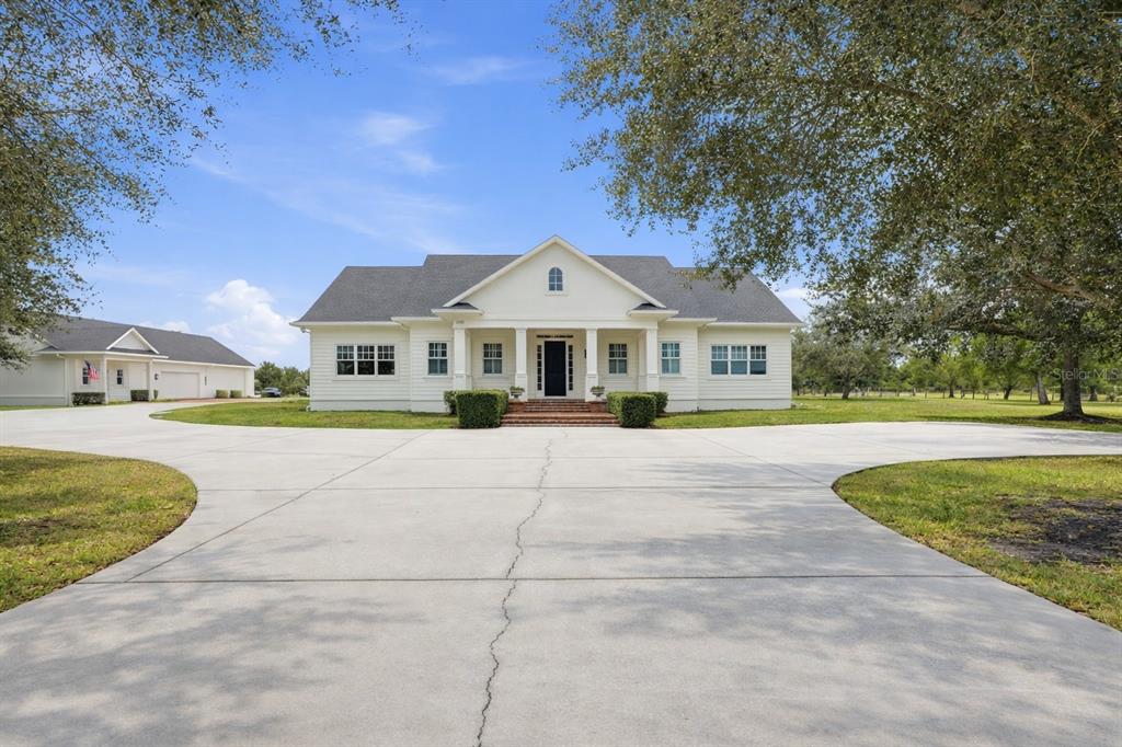 A large, white, single-story house with a dark roof sits behind a wide concrete driveway — 12201 CAISSON LANE, FORT MYERS, FL