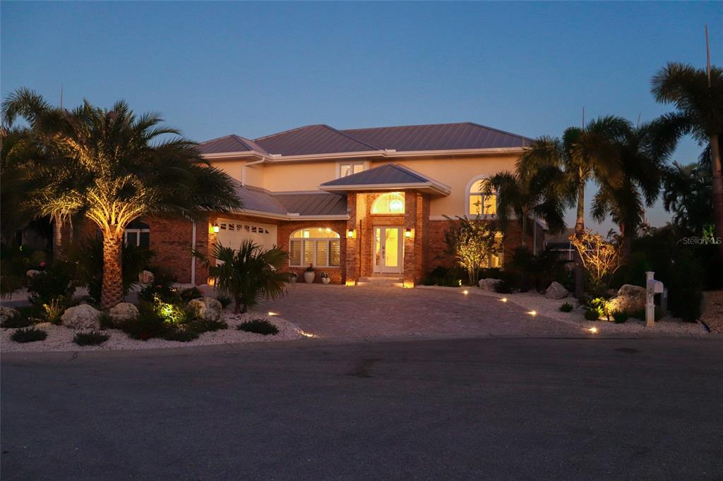 A two-story house with a brick facade, metal roof, and illuminated landscaping at dusk — 620 NORTH POINT DRIVE, HOLMES BEACH, FL