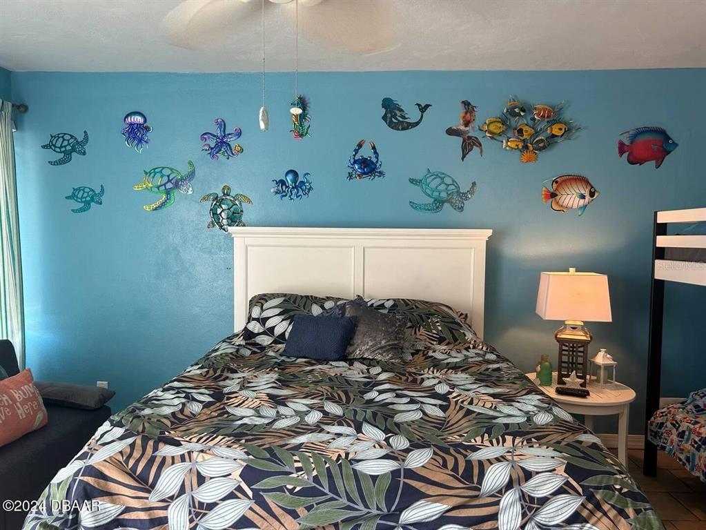 A bedroom features a bed with a tropical print comforter against a blue wall decorated with metal sea-life art — 219 S ATLANTIC AVENUE UNIT 308, DAYTONA BEACH, FL