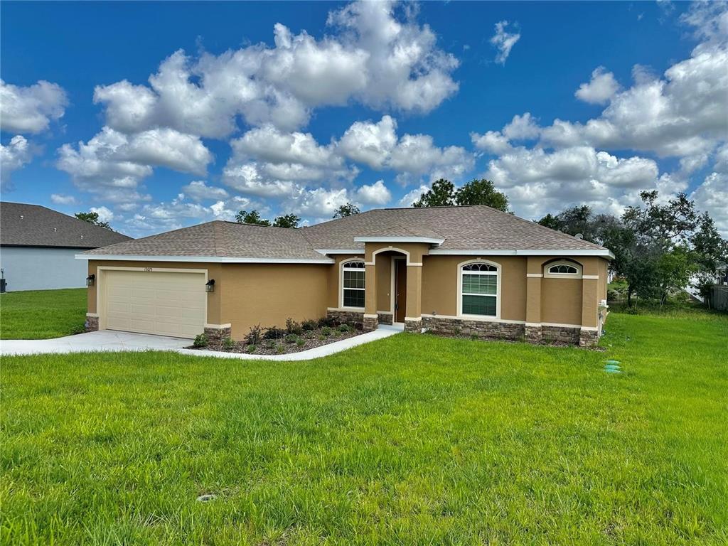 A single-story house with a tan stucco exterior, stone accents, and a two-car garage — 13075 HOUSE FINCH ROAD, WEEKI WACHEE, FL