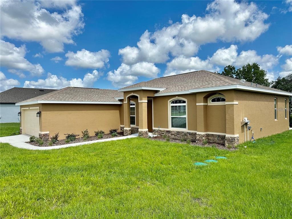A single-story tan stucco house with a stone veneer base and a two-car garage — 13075 HOUSE FINCH ROAD, WEEKI WACHEE, FL