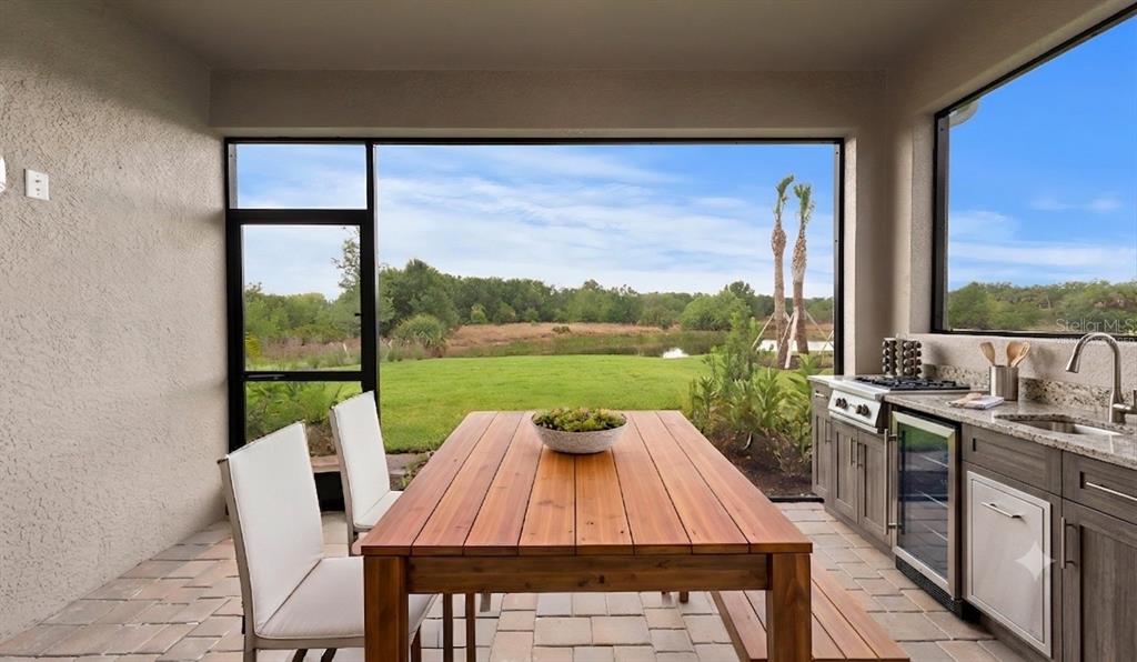 A covered patio features a wooden dining table, outdoor kitchen, and views of a grassy yard — 2949 HERITAGE PINES DRIVE, FORT MYERS, FL