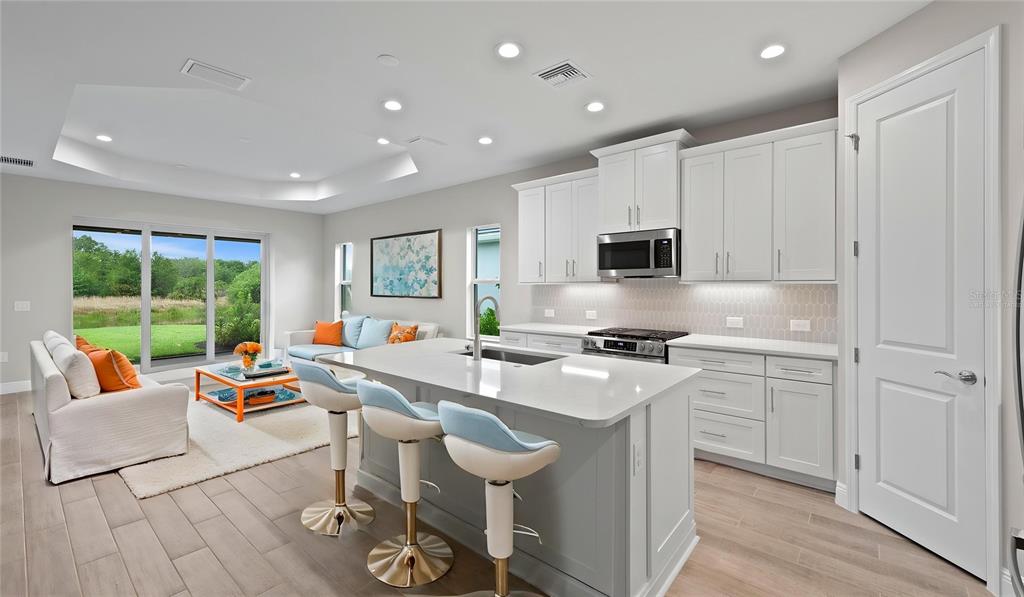 A modern kitchen with white cabinets and a central island overlooks a bright living area — 2949 HERITAGE PINES DRIVE, FORT MYERS, FL
