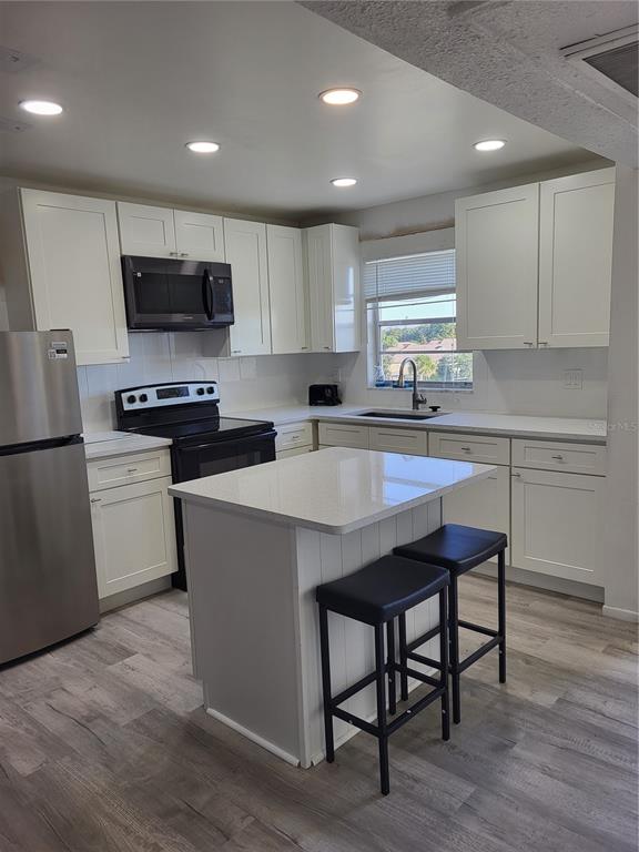 A kitchen with white cabinets, stainless steel appliances, a center island, and wood-look flooring — 4650 COVE CIRCLE UNIT 611, ST PETERSBURG, FL