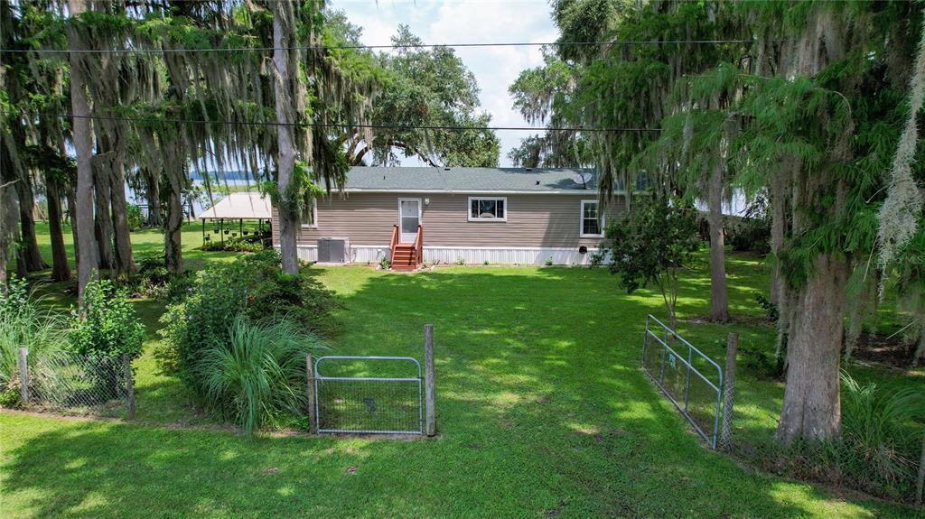 A single-story house with tan siding sits on a grassy lot surrounded by mossy trees — 9065 W LAKEVIEW COURT, CRYSTAL RIVER, FL