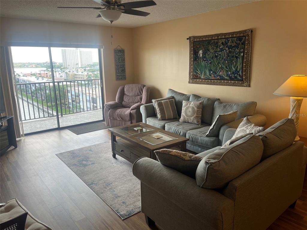 A living room features a gray sofa, coffee table, and a balcony with water views — 7300 SUN ISLAND DRIVE S UNIT 702, SOUTH PASADENA, FL