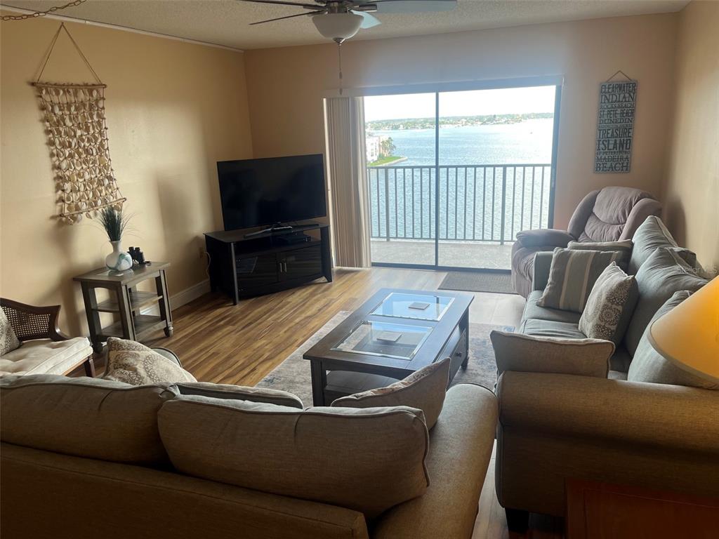 A living room features wood-look flooring, a television, a coffee table, and a balcony view — 7300 SUN ISLAND DRIVE S UNIT 702, SOUTH PASADENA, FL