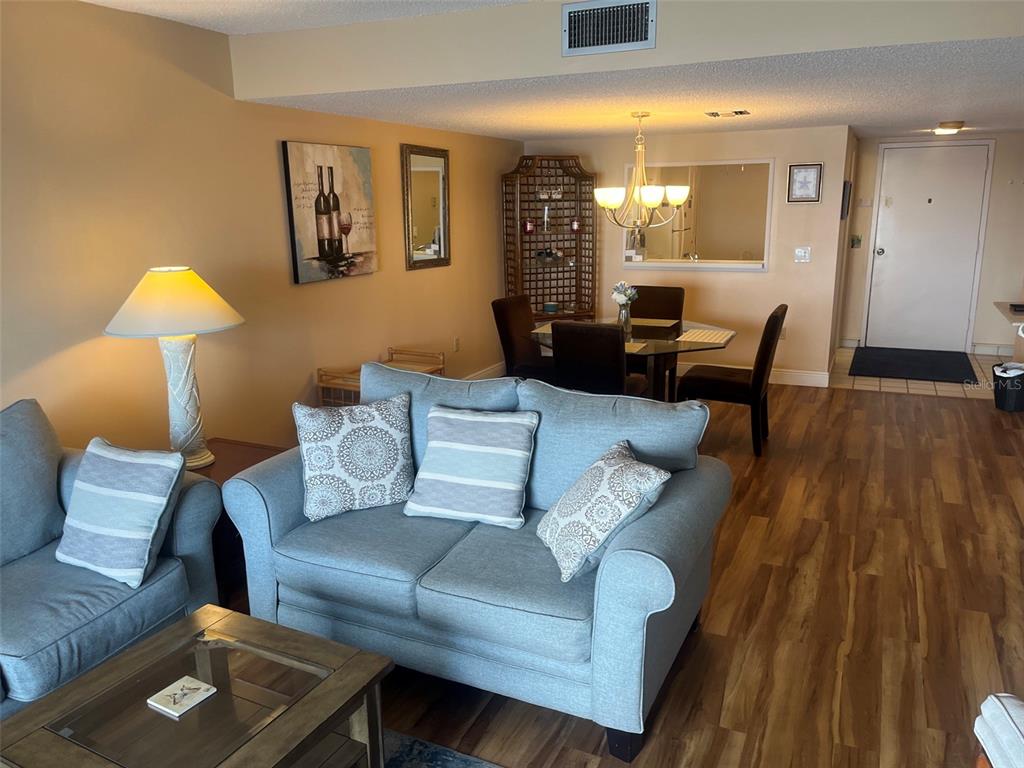 A living room and dining area feature light blue sofas, wood-look flooring, and a glass table — 7300 SUN ISLAND DRIVE S UNIT 702, SOUTH PASADENA, FL