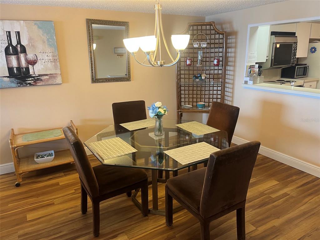 A dining room features a glass-topped table, four brown chairs, and a rattan display shelf — 7300 SUN ISLAND DRIVE S UNIT 702, SOUTH PASADENA, FL