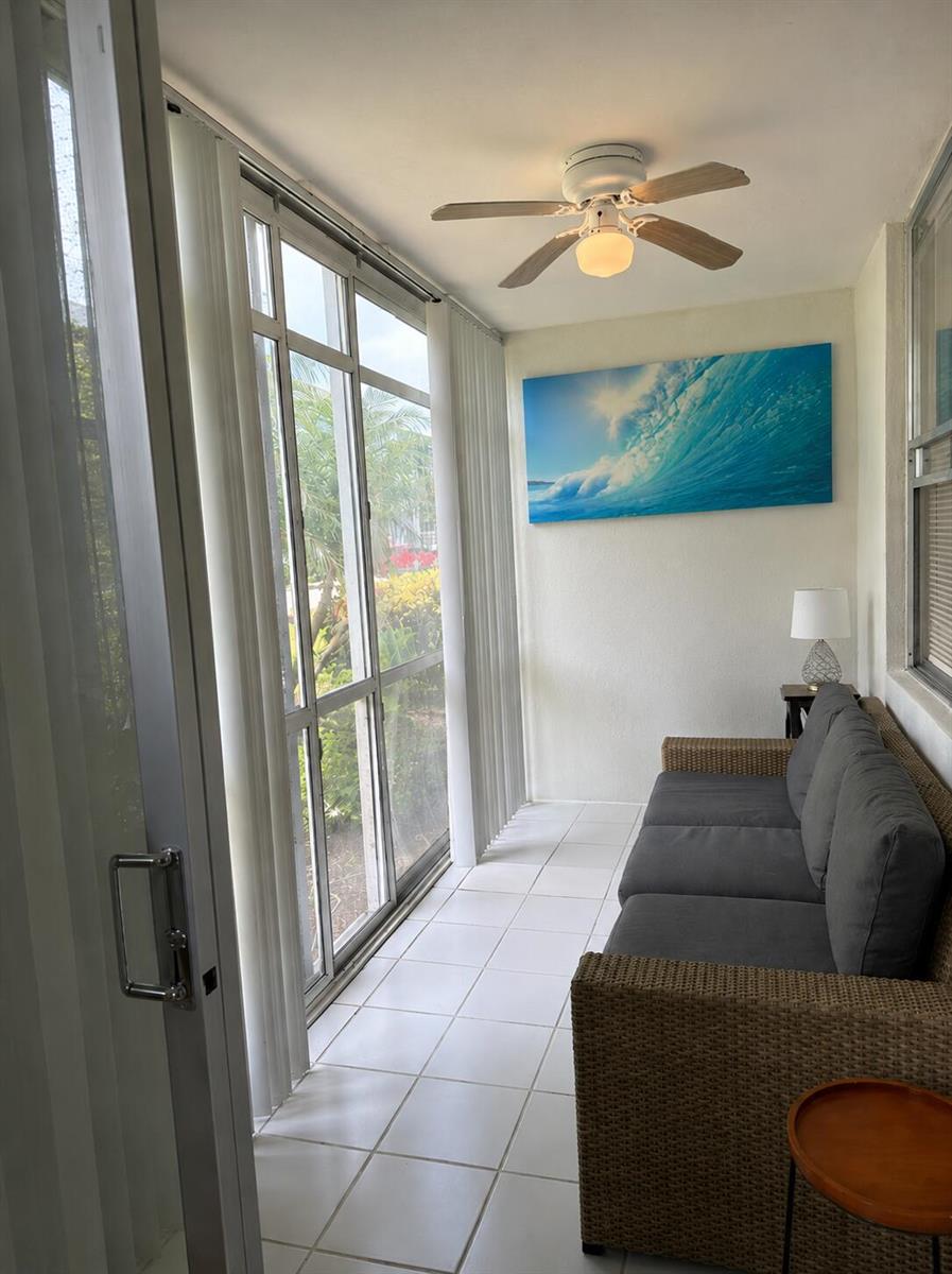 A sunroom features white tile floors, a wicker sofa, a ceiling fan, and a wave painting — 2016 S Federal Highway # 105, Boynton Beach FL 33435, BOYNTON BEACH, FL