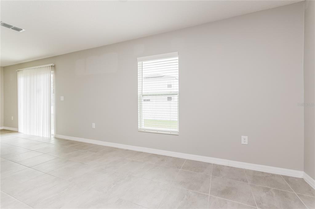 An empty room with light gray walls, tile flooring, a window, and sliding glass doors — 222 FIG COURT, KISSIMMEE, FL