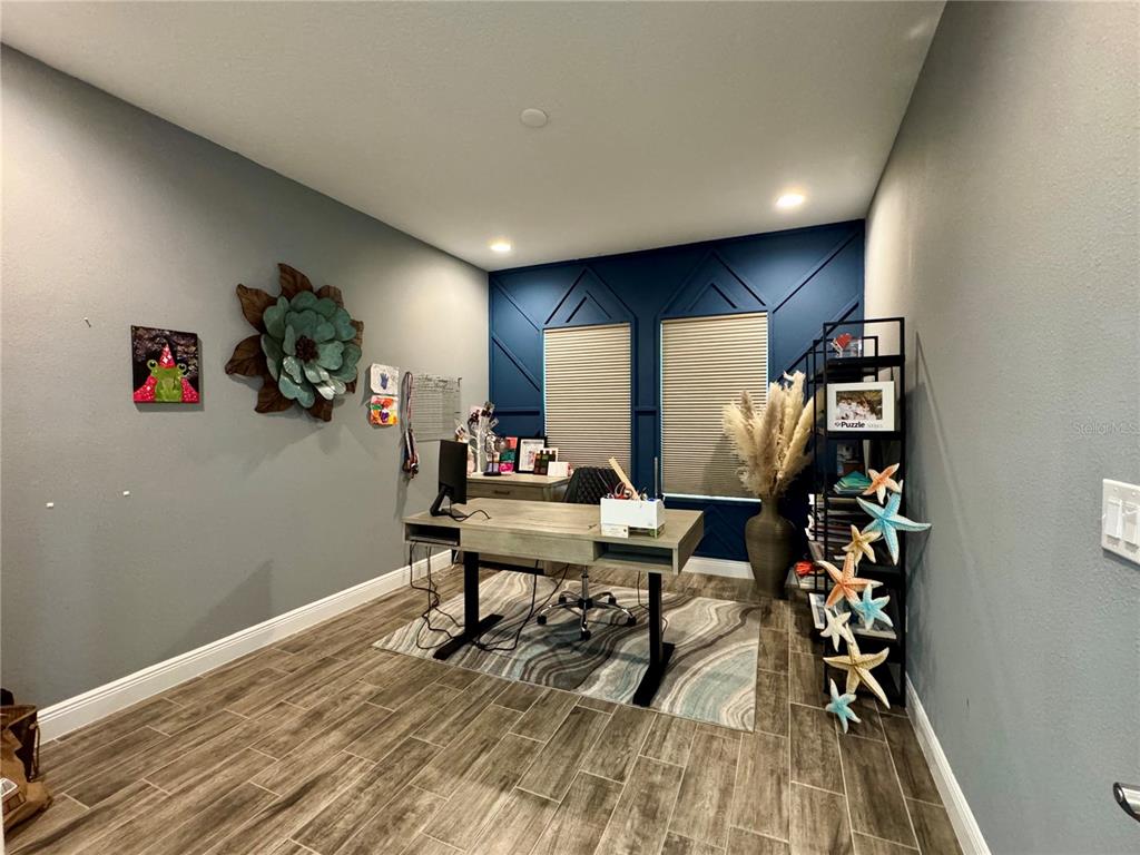 A home office features a wood desk, a blue accent wall, and wood-look tile flooring — 12870 TWIN BRIDGES DRIVE, RIVERVIEW, FL