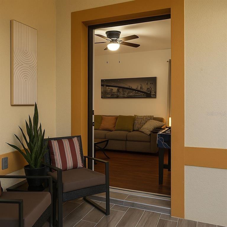 A covered patio with chairs and a plant overlooks a living room through a doorway — 438 MONROE CIRCLE, DAVENPORT, FL