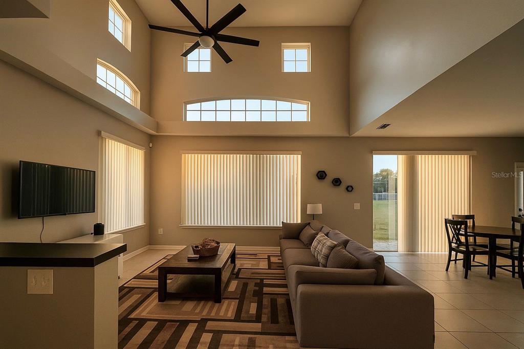 A living room with high ceilings, a ceiling fan, large windows, and a gray sofa — 438 MONROE CIRCLE, DAVENPORT, FL