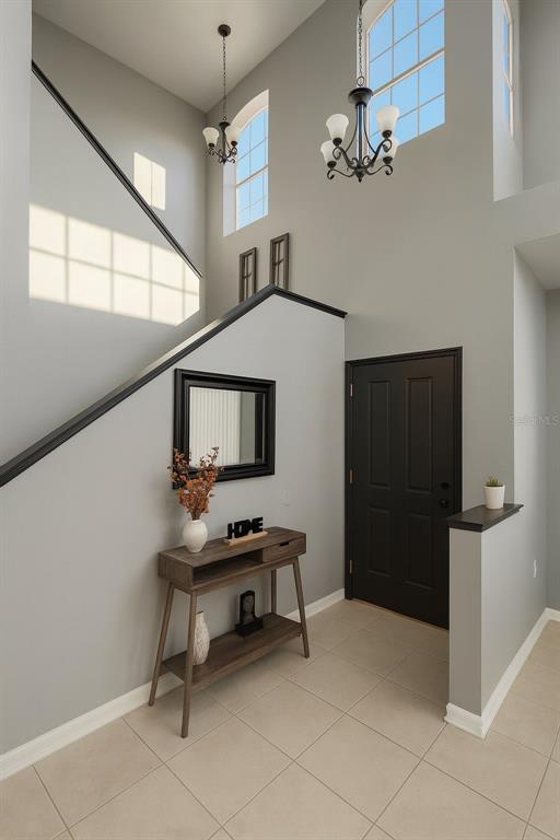A high-ceilinged foyer features a staircase with a black railing, tile flooring, and a console table — 438 MONROE CIRCLE, DAVENPORT, FL