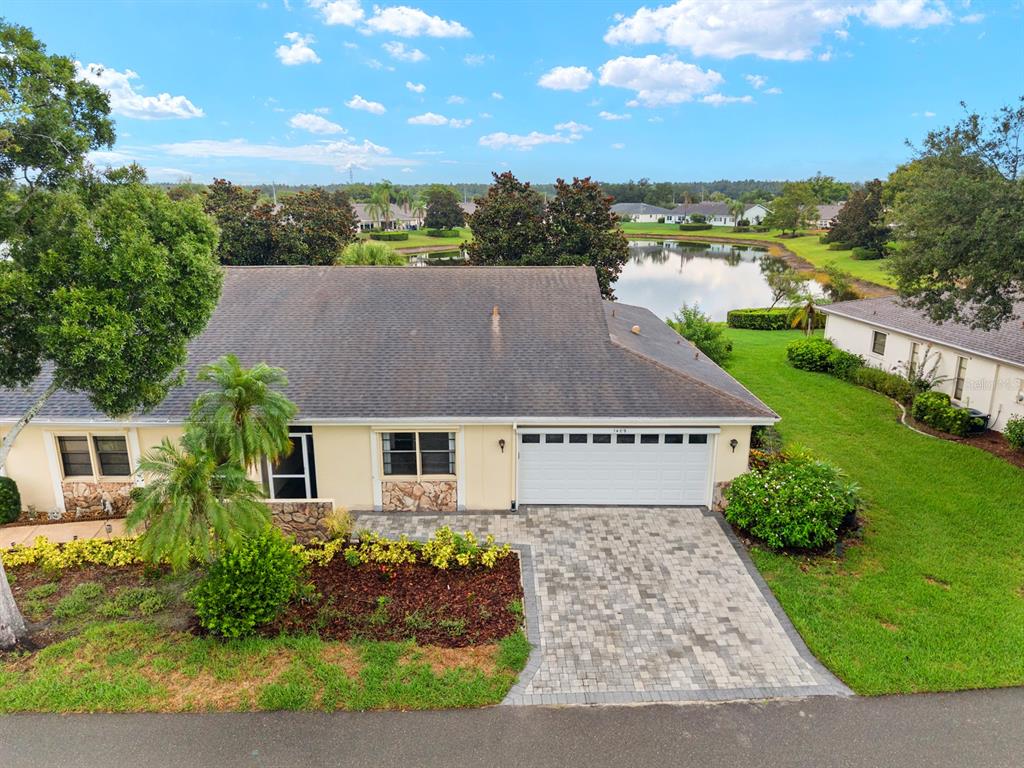 An aerial view of a single-story house with a paved driveway and a backyard pond — 1409 LANGLEY DRIVE UNIT 1409, SUN CITY CENTER, FL