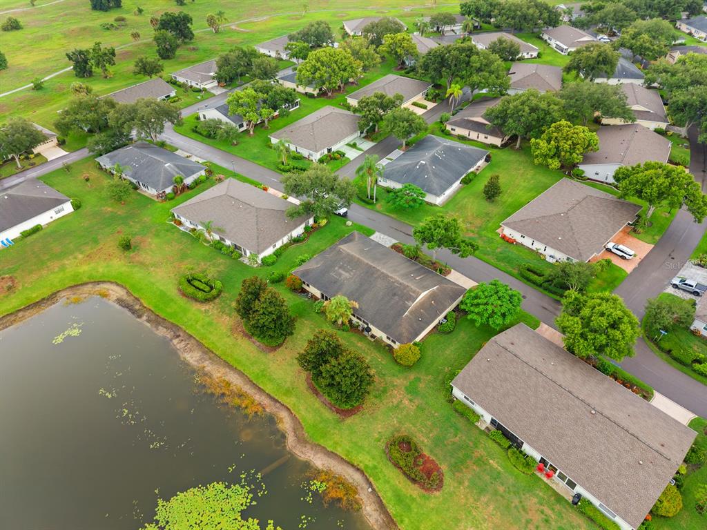 An aerial view shows multiple residential houses surrounded by green lawns and a small pond — 1409 LANGLEY DRIVE UNIT 1409, SUN CITY CENTER, FL