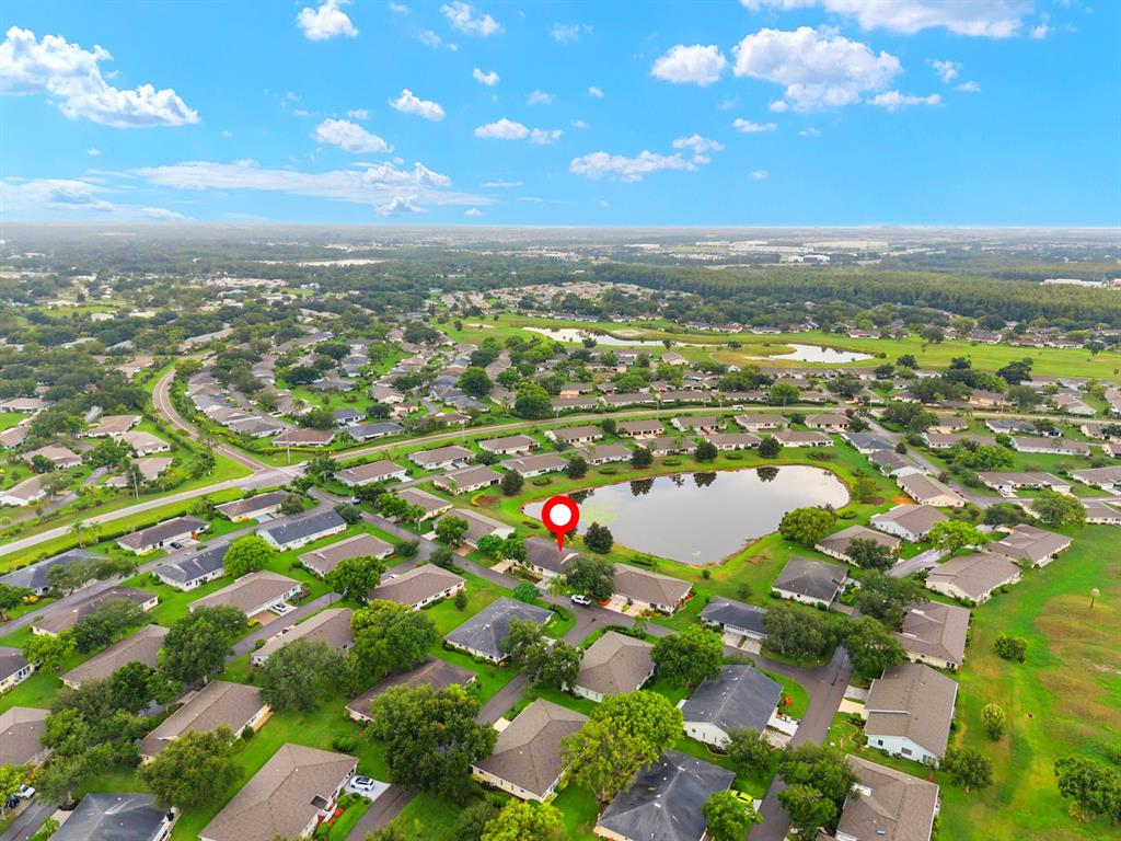 An aerial view shows a residential neighborhood with houses surrounding a central pond — 1409 LANGLEY DRIVE UNIT 1409, SUN CITY CENTER, FL