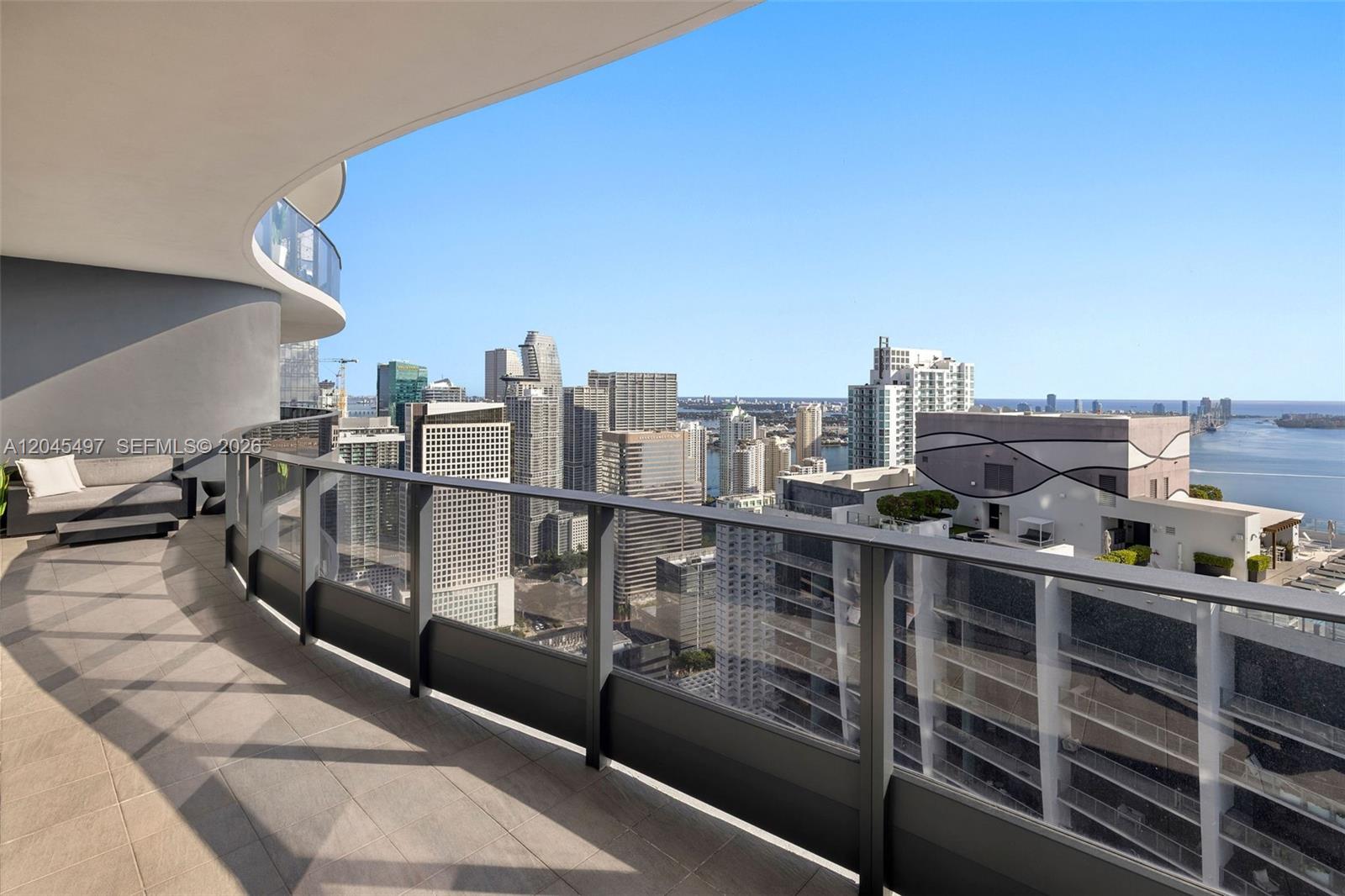 A curved balcony with glass railings overlooks a city skyline and a body of water — 1000 Brickell Plz, Miami FL 33131, MIAMI, FL