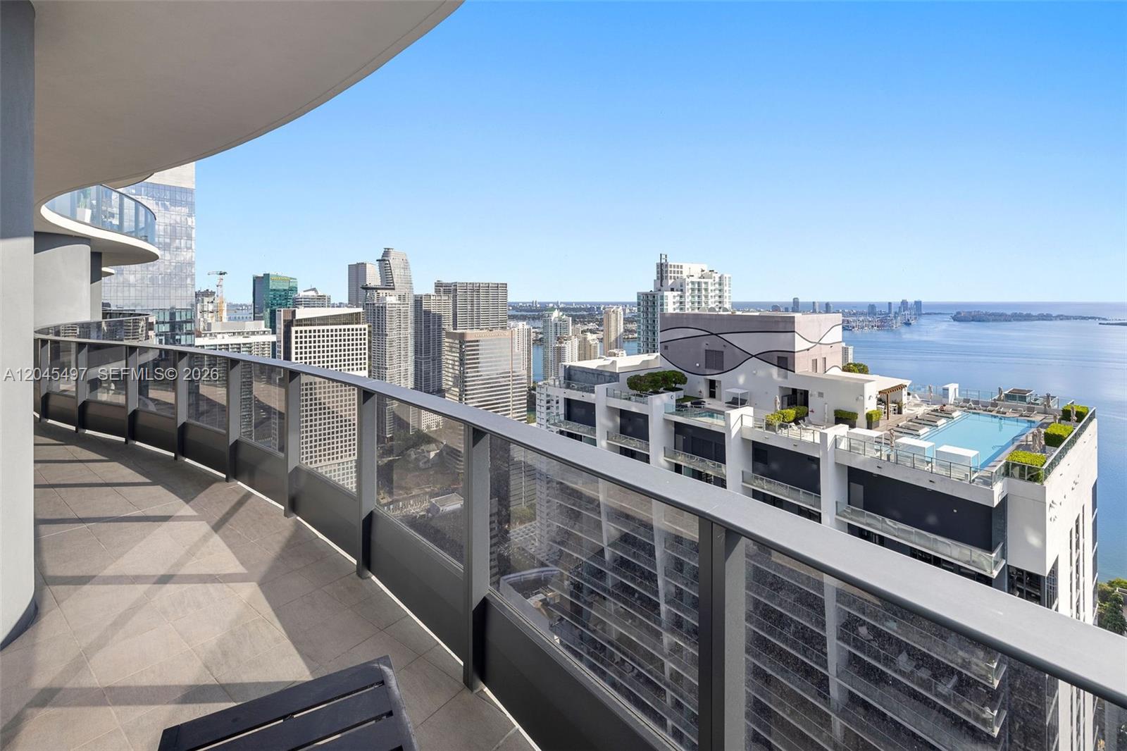 A high-rise balcony with a glass railing overlooks a city skyline and a bay — 1000 Brickell Plz, Miami FL 33131, MIAMI, FL