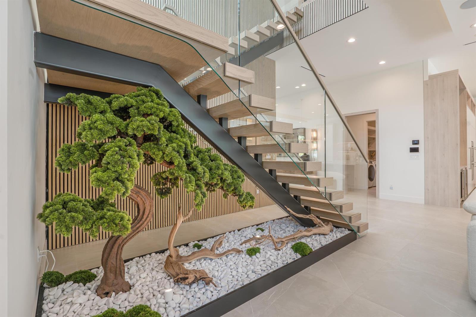 A modern staircase with glass railings sits above a decorative indoor garden with white stones — 400 NE 4th Street, Boca Raton FL 33432, BOCA RATON, FL