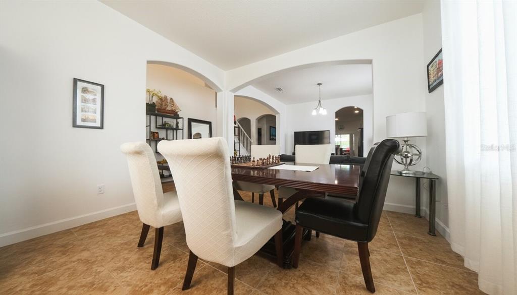 A dining room features a wooden table with a chessboard, upholstered chairs, and tiled flooring — 1903 HAILSHAM COURT, ORLANDO, FL