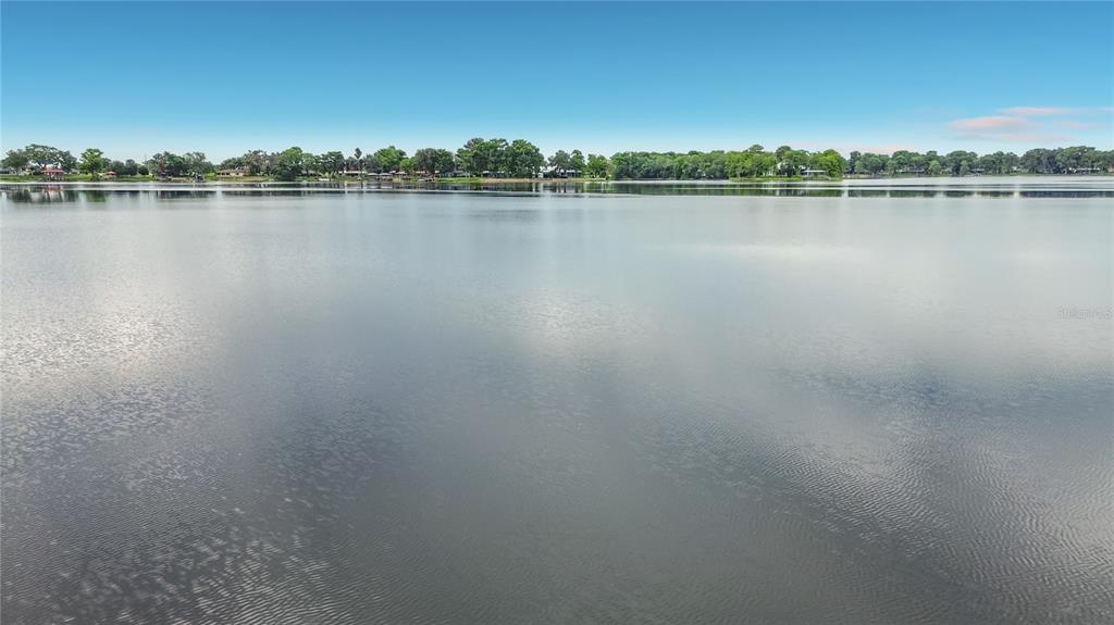 A wide, calm lake stretches toward a distant tree-lined shore under a clear blue sky — 8980 E DEVILSNECK ROAD, FLORAL CITY, FL