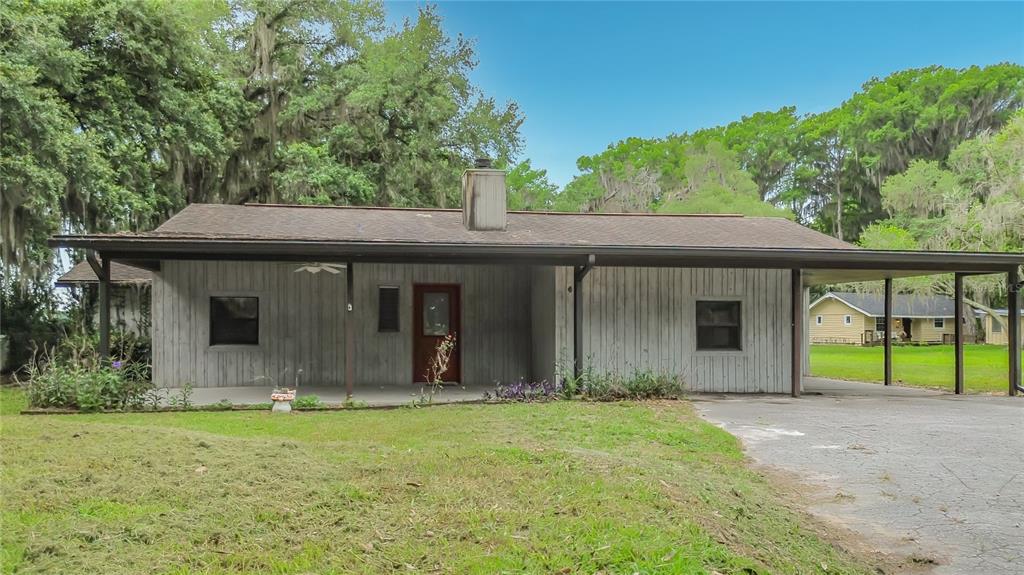 A single-story house with vertical wood siding, a covered front porch, and an attached carport — 8980 E DEVILSNECK ROAD, FLORAL CITY, FL