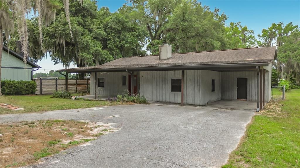 A single-story house with a large carport, gray vertical siding, and a paved driveway — 8980 E DEVILSNECK ROAD, FLORAL CITY, FL