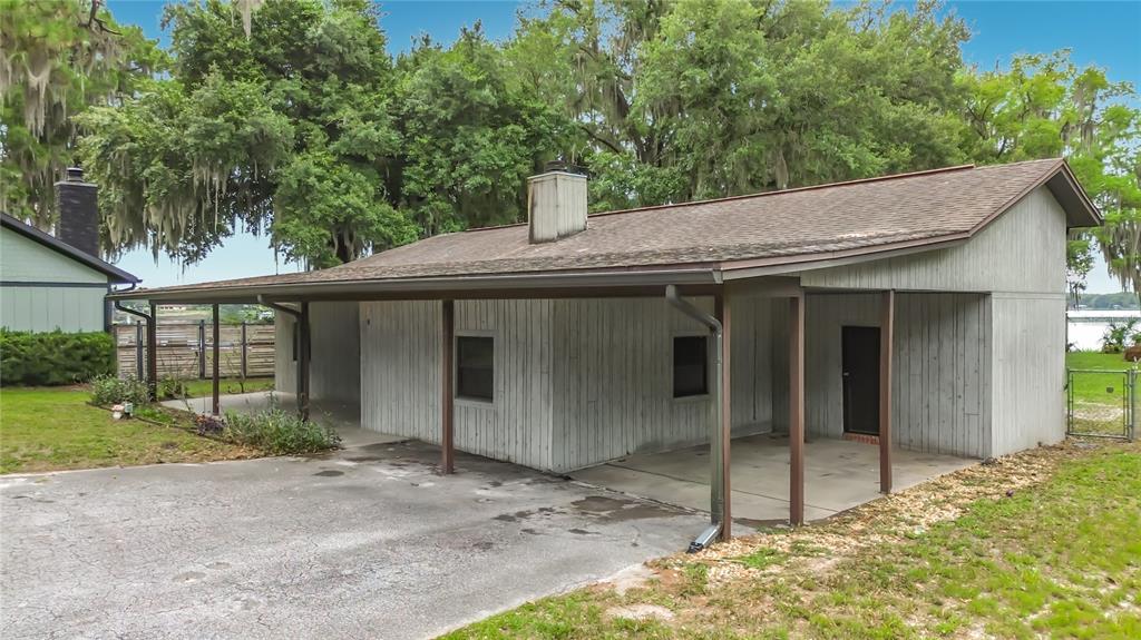 A single-story house with gray vertical siding, a covered carport, and a metal chimney — 8980 E DEVILSNECK ROAD, FLORAL CITY, FL