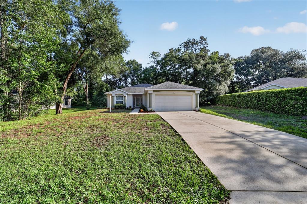 A single-story house with a two-car garage and a concrete driveway sits on a lawn — 19369 SW 100TH LOOP, DUNNELLON, FL