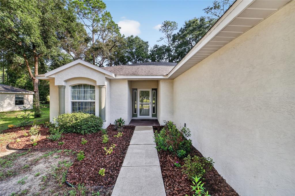A concrete walkway leads to the front entrance of a single-story home with stucco siding — 19369 SW 100TH LOOP, DUNNELLON, FL