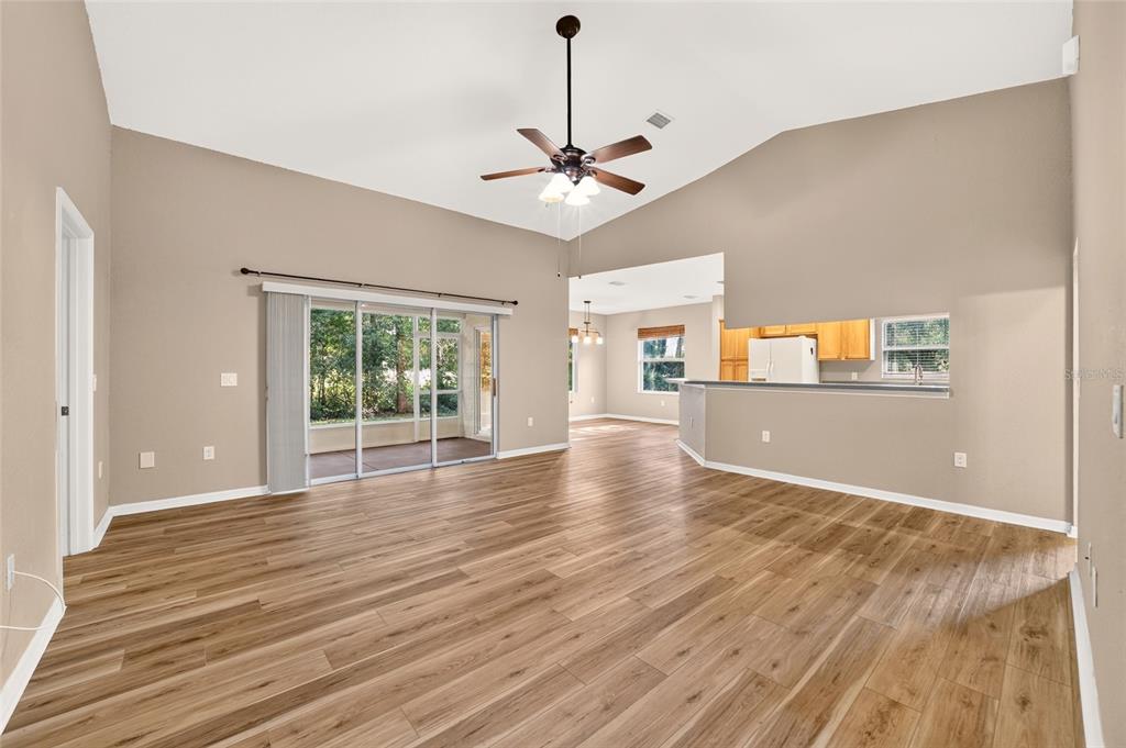 A spacious living room features wood-look flooring, a vaulted ceiling with a fan, and sliding doors — 19369 SW 100TH LOOP, DUNNELLON, FL