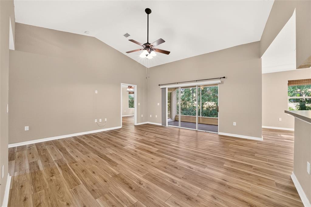 An empty living room features vaulted ceilings, a ceiling fan, and wood-look flooring — 19369 SW 100TH LOOP, DUNNELLON, FL